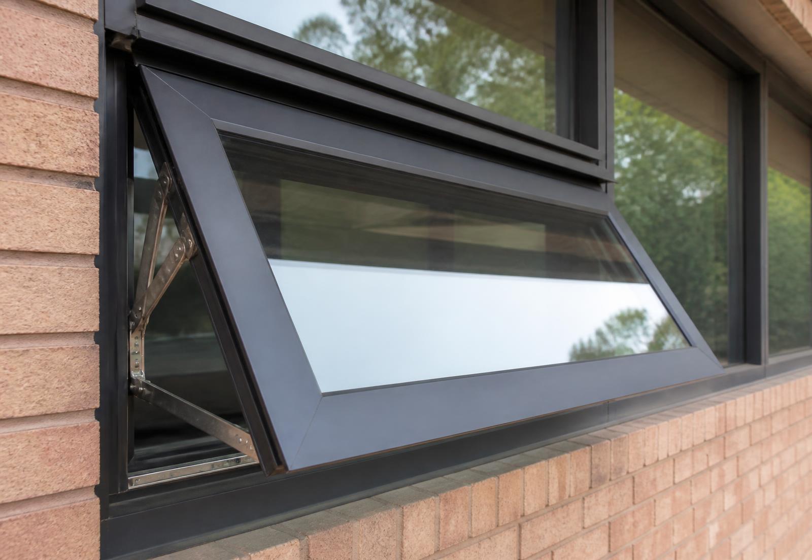 Commercial projected aluminum window open outward on stainless four-bar arms in a brick wall